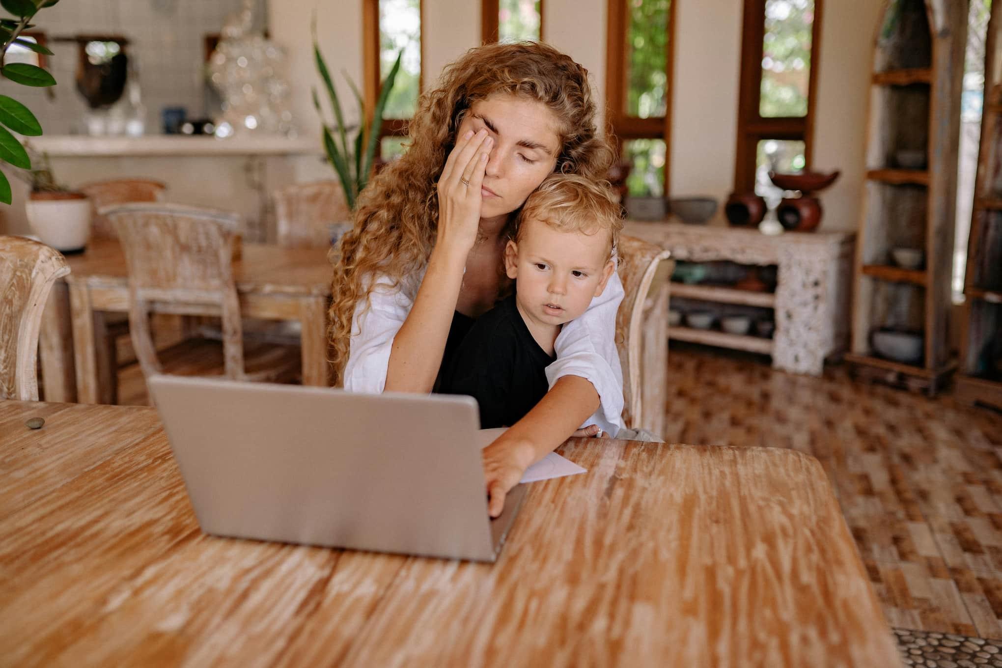 A person rubbing their eyes and looking over their computer screen